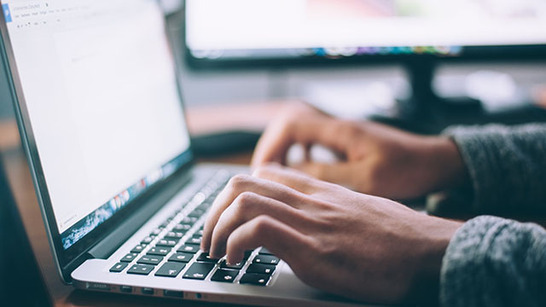 A man's hands typing on a laptop keyboard