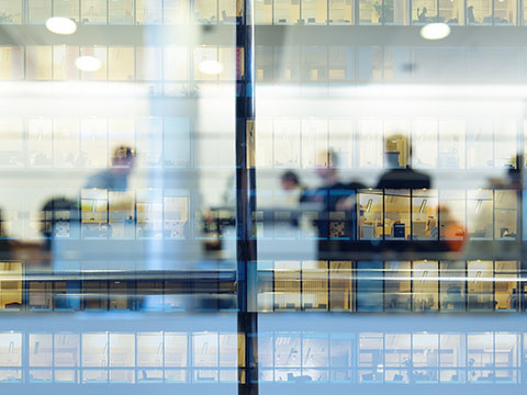 Office workers silhouetted behind a glass walled building