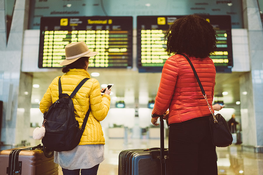 Two young female travellers look at an arrivals board in a terminal building