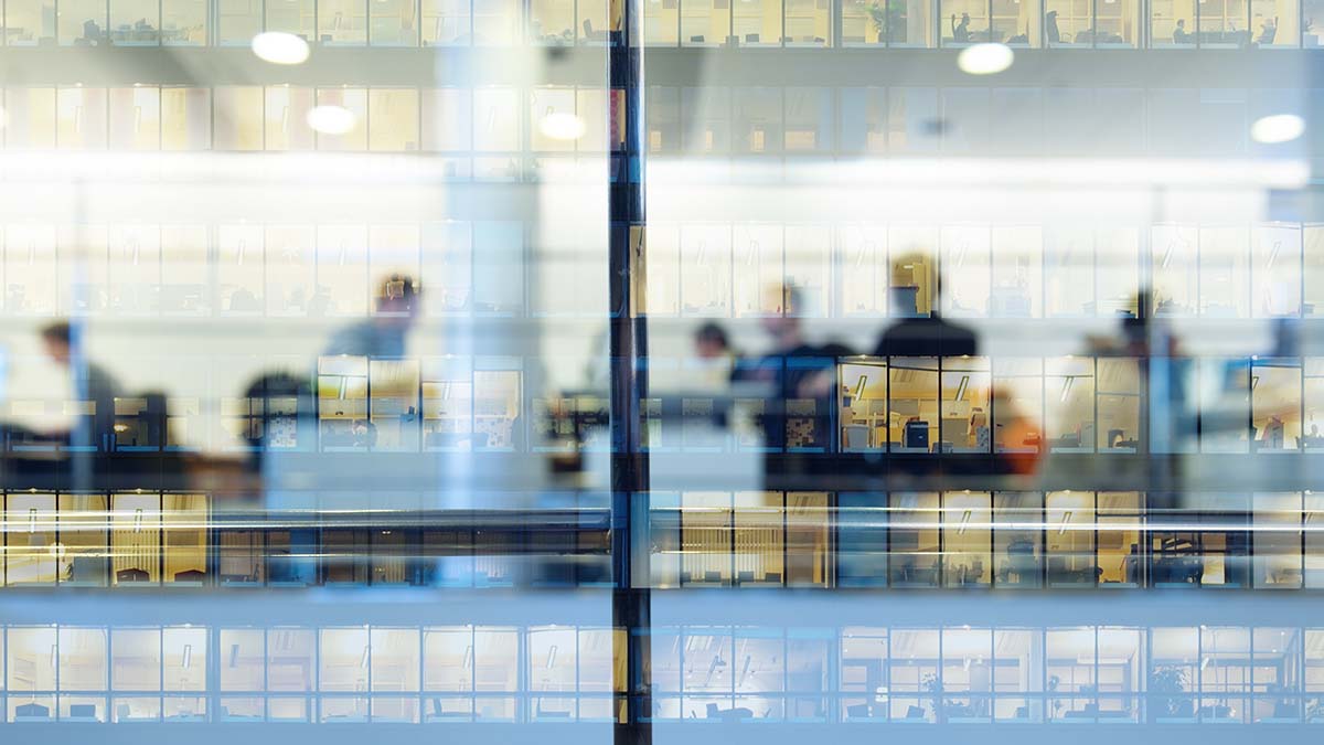 Office workers silhoutted through a glass fronted building