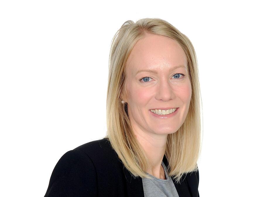 A white woman with medium-length blonde hair smiles in front of a white background