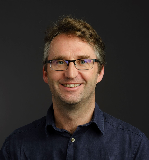 A white man with glasses and short brown hair smiling