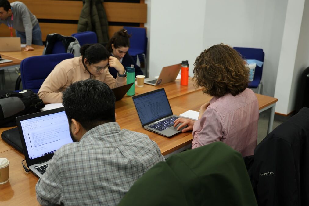 Four students around a desk working on laptops