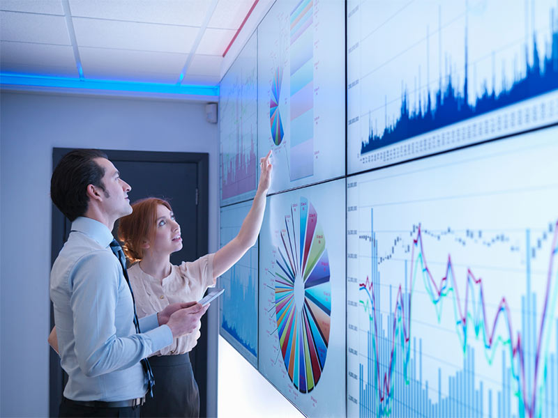 a man and woman discussing graphs displayed on a wall