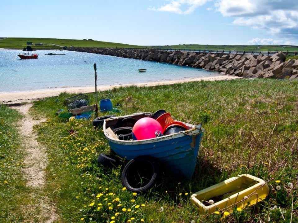 A row boat laden with fishing baskets and a pink buoy on a beach in Orkney
