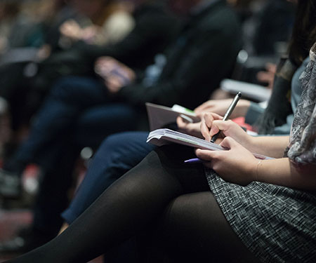 A woman takes notes in a notebook seated at an event