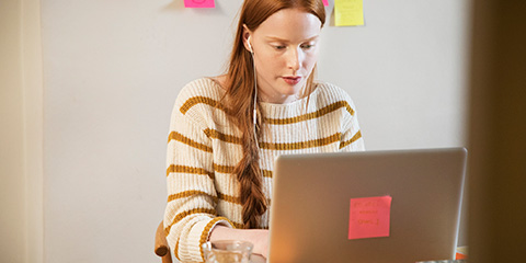 Woman using a laptop with a post-it note stuck to the lid