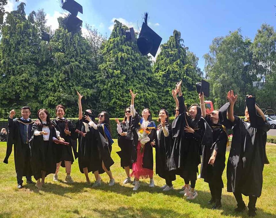 A group of Heriot-Watt students at Graduation in their robes throwing their caps and smiling
