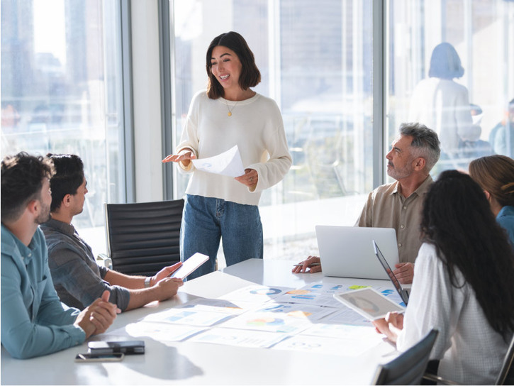 A woman stands to present in an office meeting