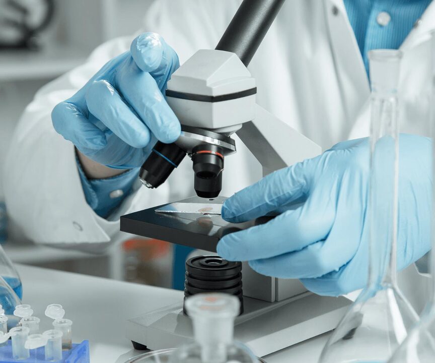 hands wearing blue gloves putting a sample slide under a microscope