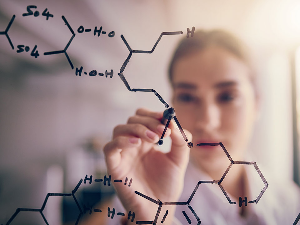 Young female scientist solving chemical equations on a glass board