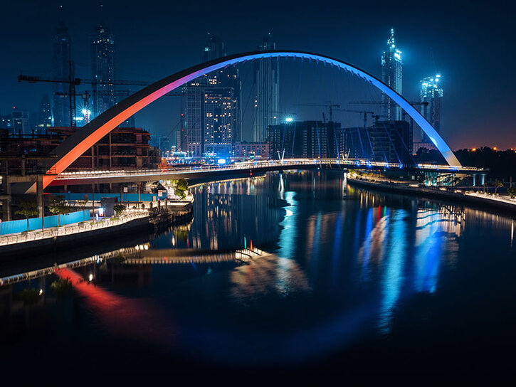 a road bridge at night. The side barriers are a semi-circle and lit blue and red