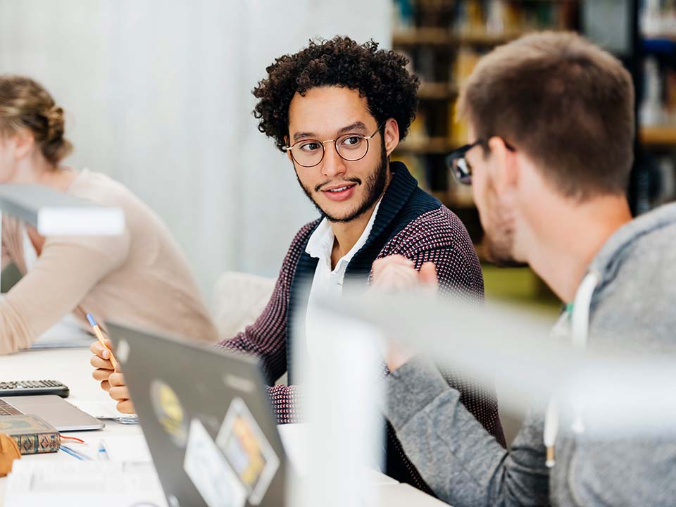 Two male students in discussion while seated at desks in a library