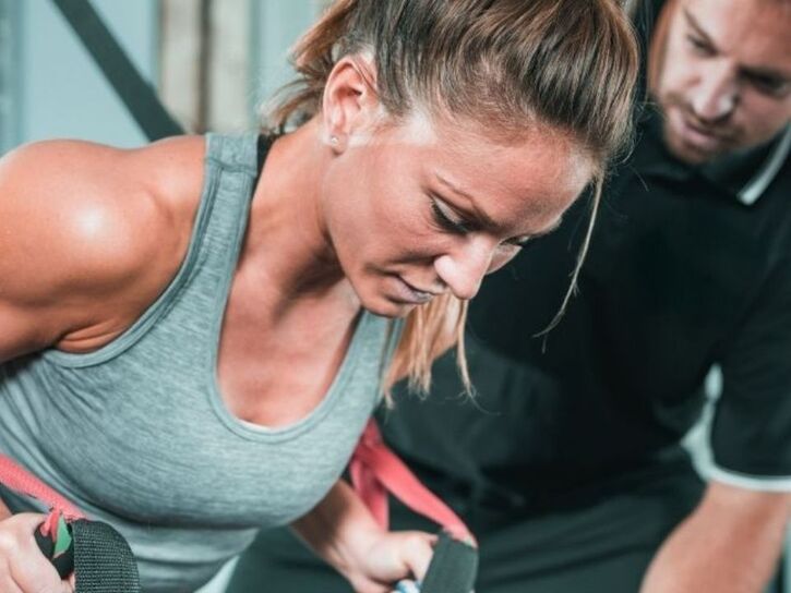 Woman doing resistance training while her personal trainer monitors her progress