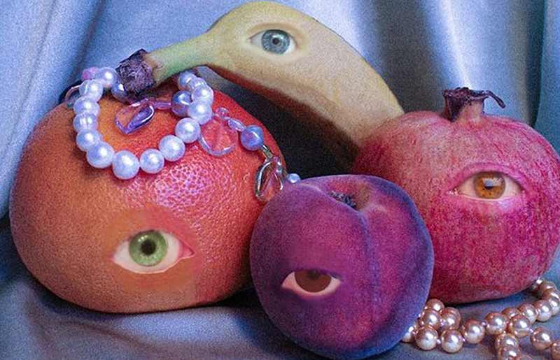 pearl necklace laid over an orange, pomegranate, peach and banana with one eye edited on each 