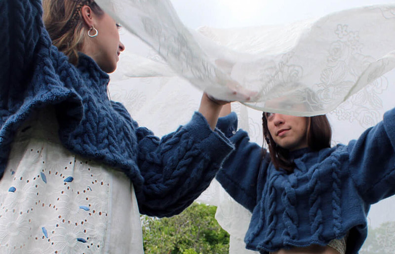 two female wearing cropped navy knitted jumpers and holding a lace sheet over heads