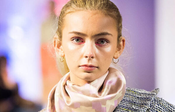headshot of model with sleeked back hair, wearing a tweed jacket and pink silk scarf