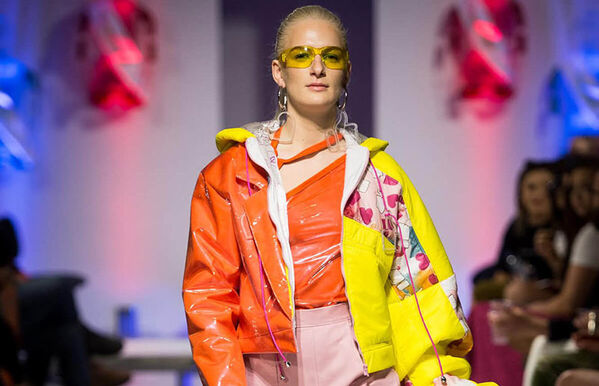 female model walking catwalk, wearing a half orange and half yellow bomber jacket, the yellow sleeve is oversized and has love heart print patchwork