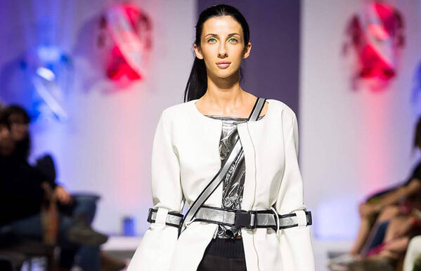 female model walking catwalk, wearing a white blazer with silver straps - like a seatbelt