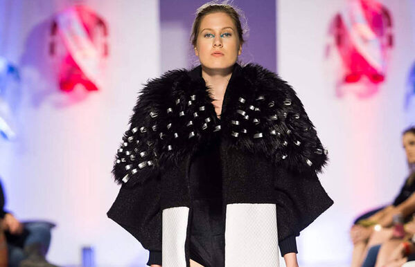 female model walking catwalk, wearing an oversized black fur shawl over a black and white geometric print coat
