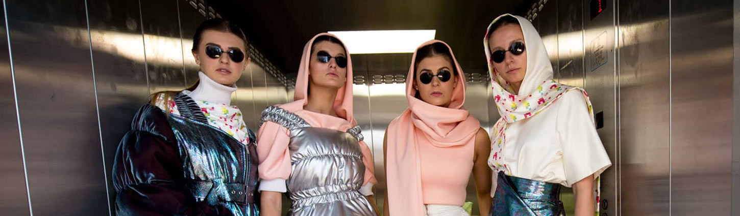four female models all wearing pink and white headscarf's with matching coloured tops. Two are wearing blue and silver metallic dresses overtop