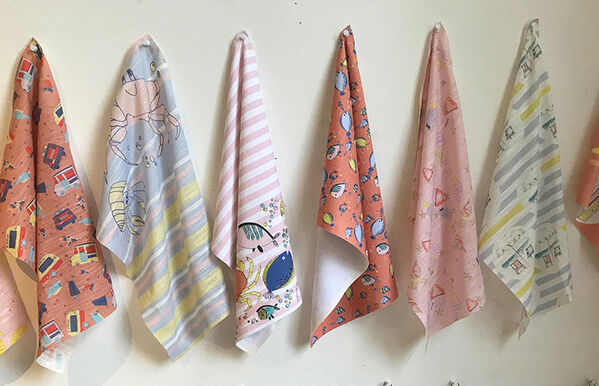 six coral, baby blue, pink and yellow sea-side themed fabric swatches handing on wall