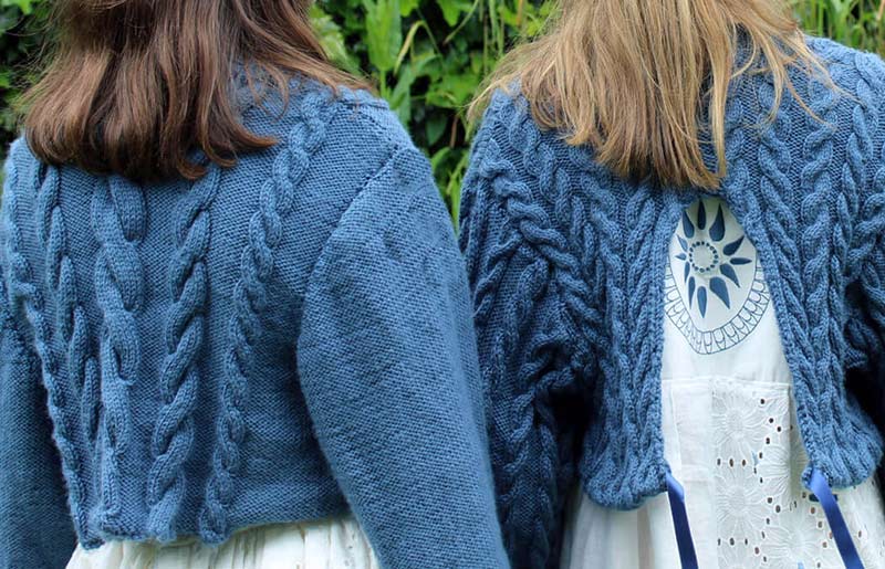 backs of two females, both wearing cropped knitted blue cardigans