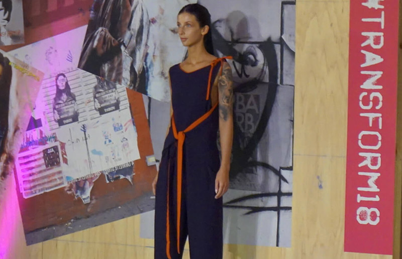 model posing in front of wall, wearing a sleeveless navy jumpsuit that is tied at the shoulders and waist with orange bows