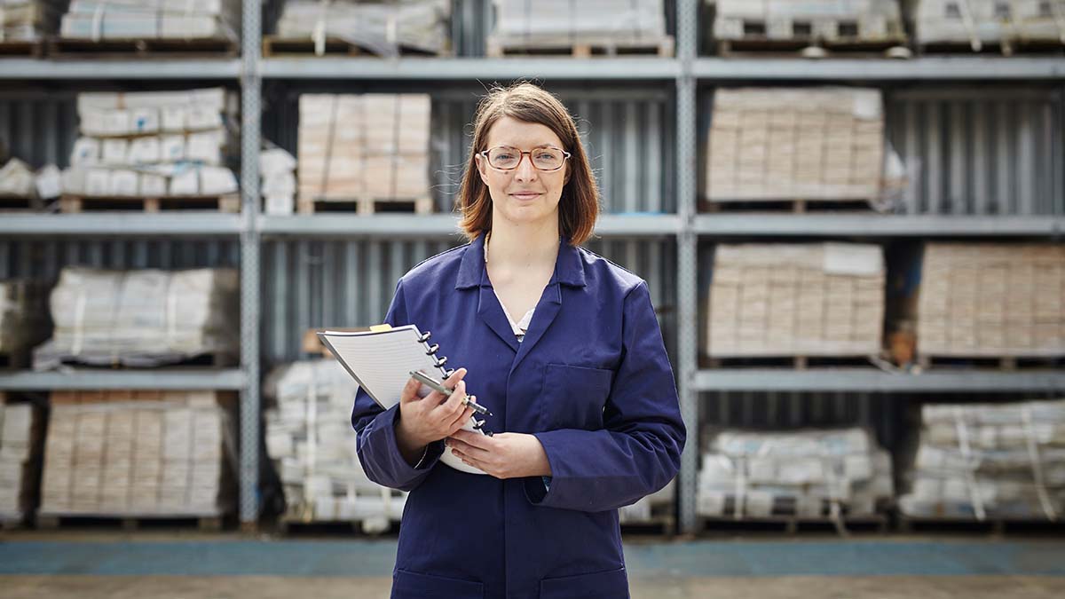 A woman engineer in blue overalls holding a clipboard standing in a goods yard