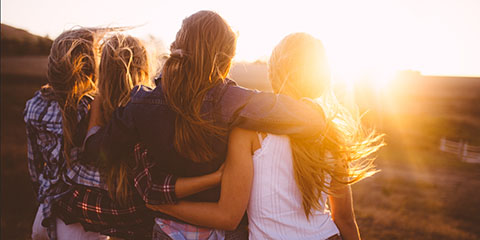 Group of young women standing in a field looking at the sunset