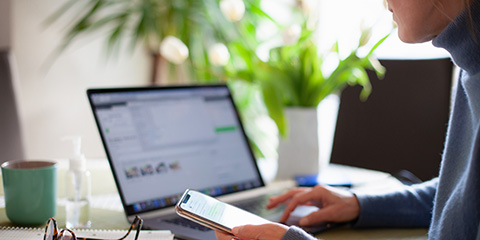 Woman checking her mobile phone while working at her laptop